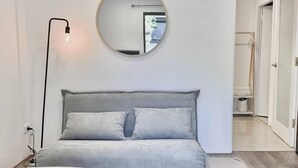 A modern living room with a grey sofa, a round mirror, and a white ottoman. - PP Garden (Bondi)
