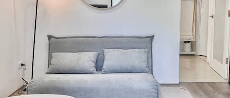A modern living room with a grey sofa, a round mirror, and a white ottoman.