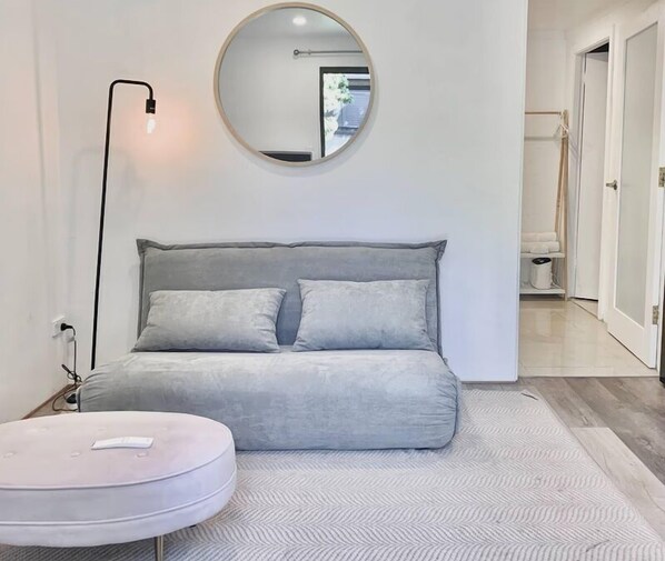 A modern living room with a grey sofa, a round mirror, and a white ottoman.