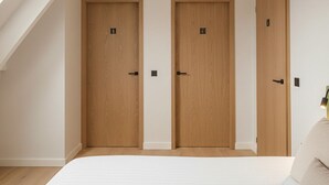 Een slaapkamer met een schuine hemel, twee houten deuren, een bed met witte beddengoed en een klein raam.
