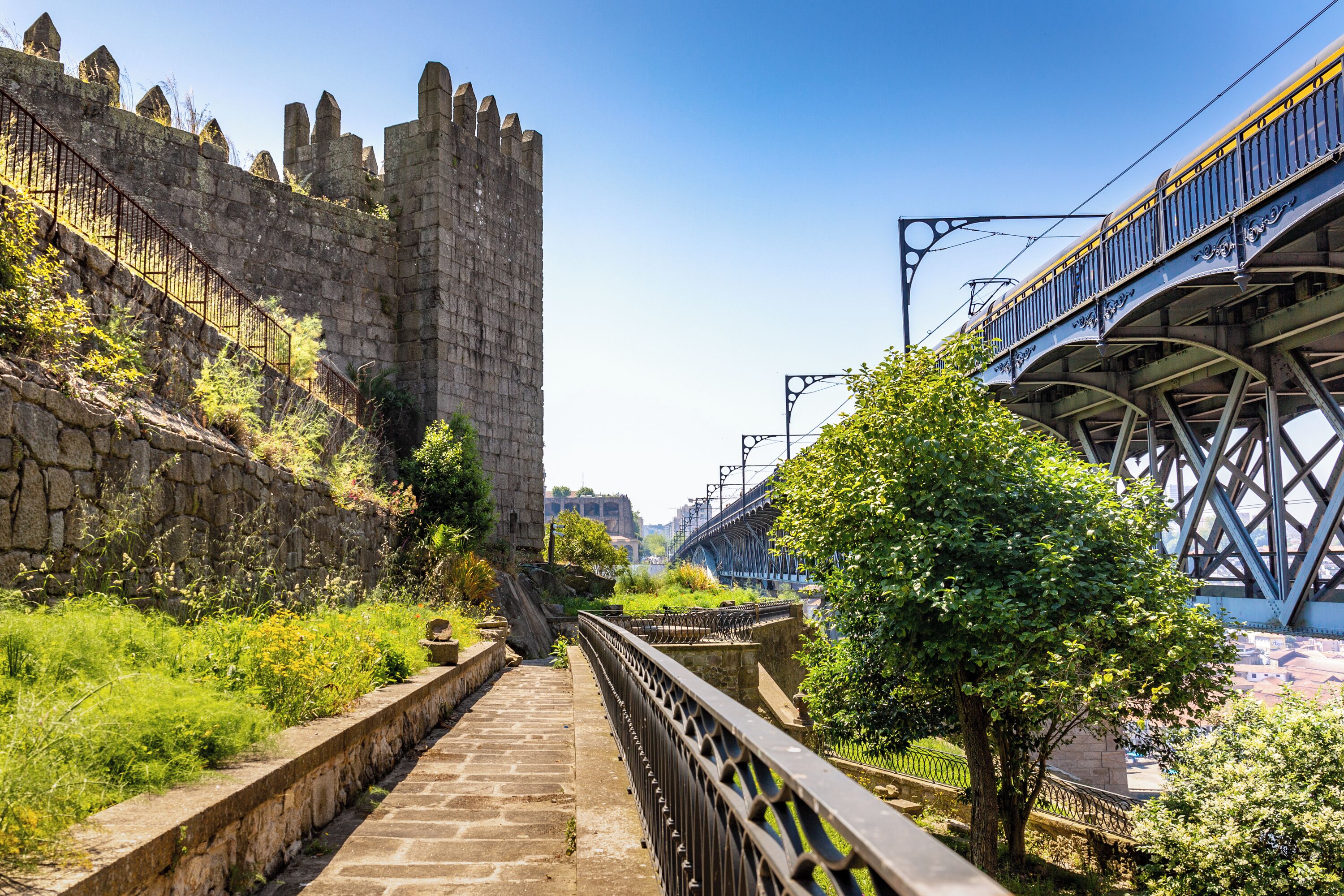 Un sentier de pierres mène à un château historique, avec un pont et des voies ferrées à proximité.
