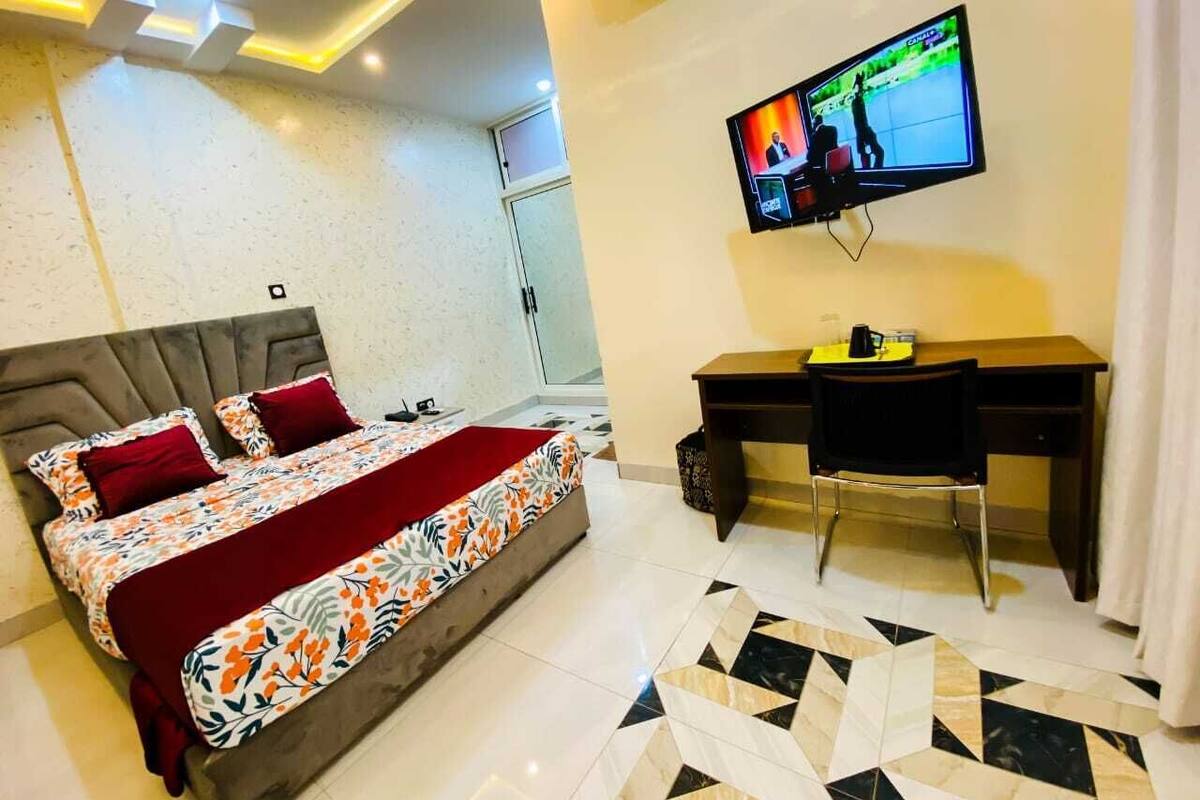 Ein Hotelzimmer mit Bett, Schreibtisch, Stuhl, Fernseher und einem gemusterten Teppich.