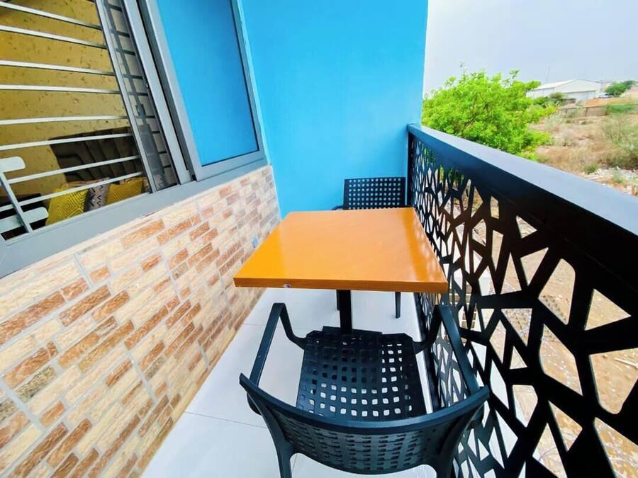 A balcony with a table and chairs, a blue wall, and a view of greenery and buildings in the background.