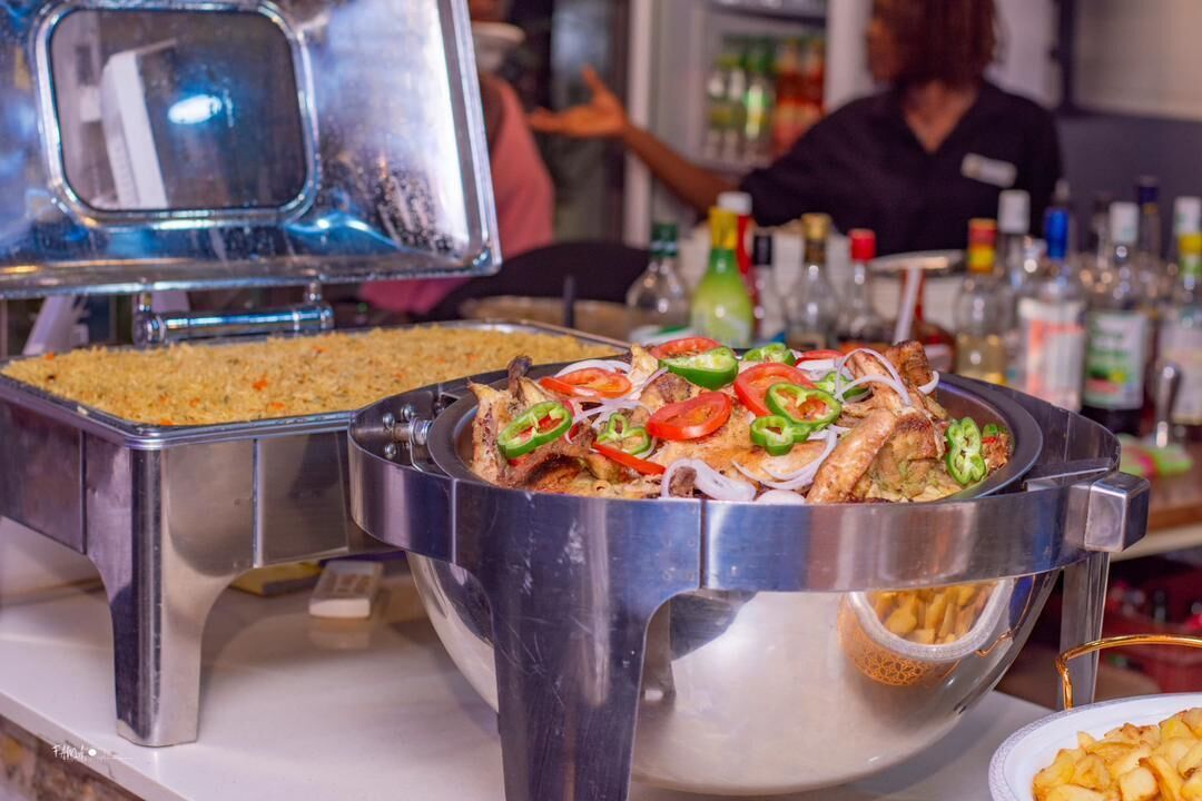 A buffet setup with various food items, including rice, grilled chicken, and sliced vegetables.