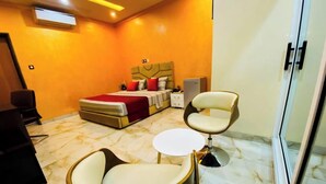 Una habitación de hotel con cama, dos sillas, una mesita pequeña y un minibar.