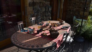 Ein runder Gartentisch mit Fliesenplatte, umgeben von Metallstühlen, auf einer Holzterrasse mit Steinmauern im Hintergrund.