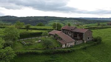 A stone farmhouse with a large barn, surrounded by lush green fields and rolling hills.