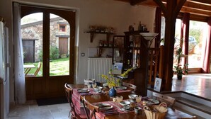 Ein Essbereich mit einem Tisch für vier Personen, einer hölzernen Bank, einem Heizkörper und Blick auf den Garten durch eine offene Tür.