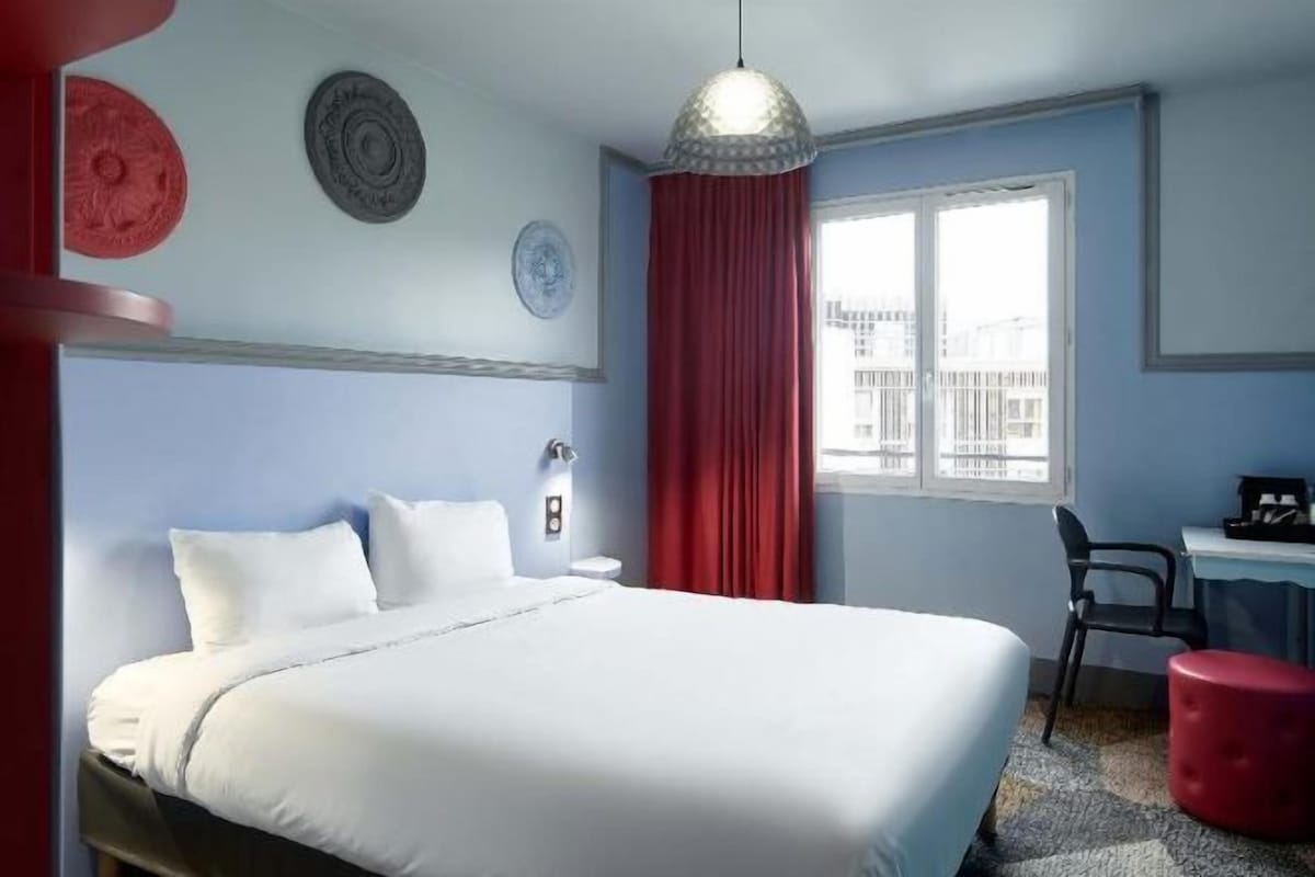 A hotel room with a bed, a desk, a chair, and a window with a view.