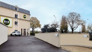 A B&B hotel with a parking sign, a white car, and a clear sky. - B&B Hotel Saint-maur Créteil (Saint-Maur-des-Fosses)