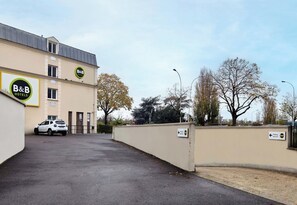 A B&B hotel with a parking sign, a white car, and a clear sky. - B&B Hotel Saint-maur Créteil (Saint-Maur-des-Fosses)