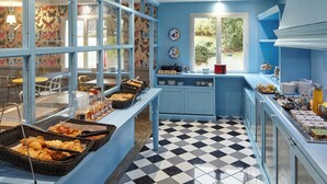A breakfast buffet with various food items, a checkered floor, and a window with a view of greenery. - B&B Hotel Saint-maur Créteil (Saint-Maur-des-Fosses)