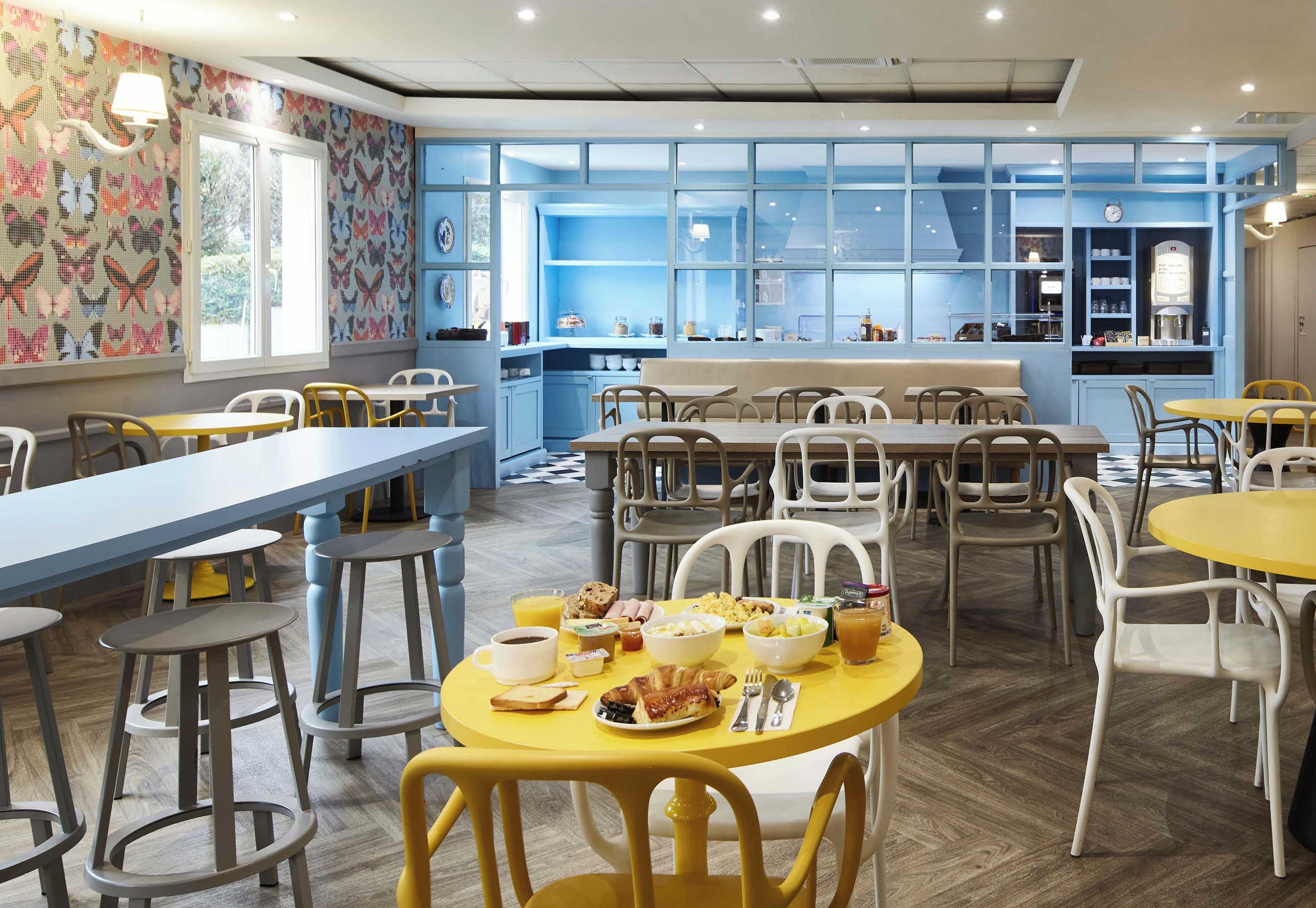 A dining area with tables and chairs, a breakfast buffet, and a kitchen area visible through the windows.