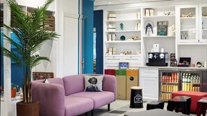 A modern interior with a purple sofa, a large potted plant, a coffee machine, and a refrigerator stocked with beverages. - B&B Hotel Saint-maur Créteil (Saint-Maur-des-Fosses)