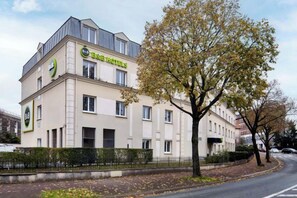 A multi-story building with a flat roof, a prominent logo on the facade, and a tree in front. - B&B Hotel Saint-Maur Créteil (Saint-Maur-des-Fosses)