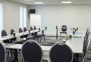 Un salón de conferencias con una pizarra, mesas, sillas y un proyector.