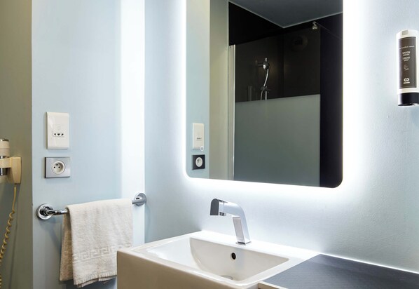 A bathroom with a white sink, a towel hanging on the wall, a mirror, and a shower visible in the background. - B&B Hotel Saint-maur Créteil (Saint-Maur-des-Fosses)