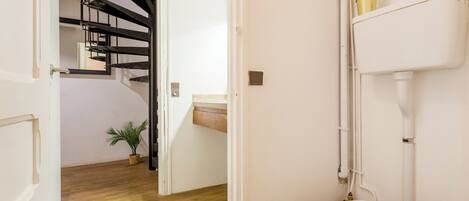 A modern bathroom with a white toilet, a wooden floor, a black spiral staircase, and a small potted plant.