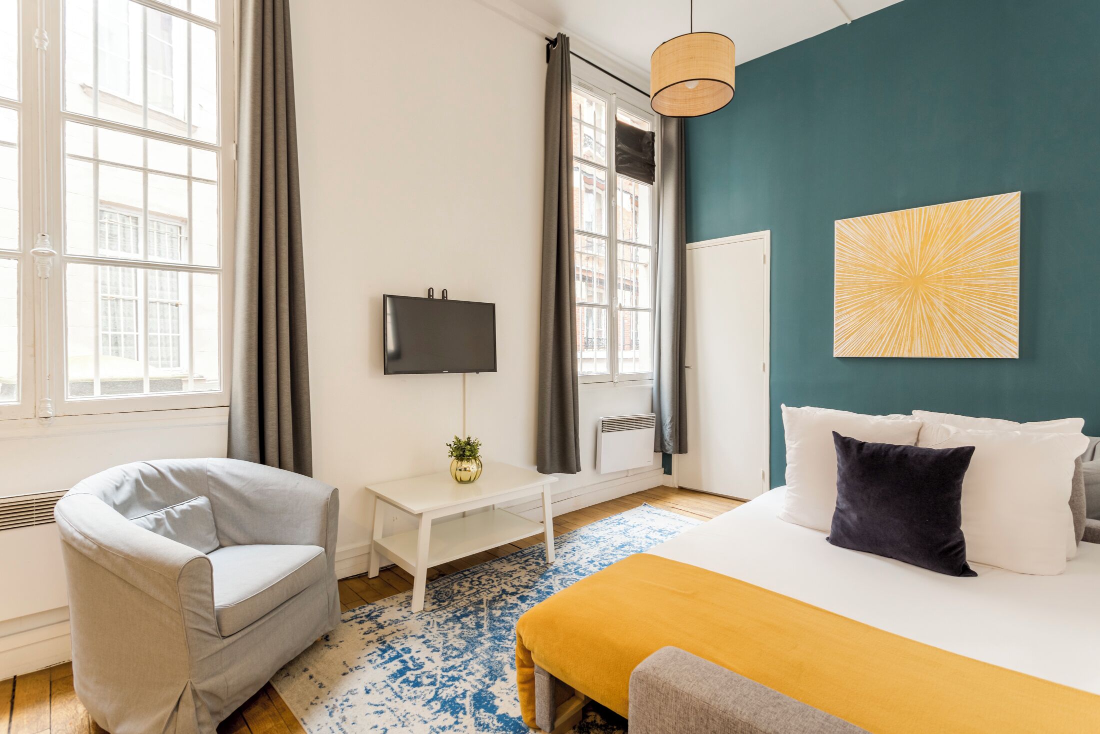 A modern hotel room with a bed, a sofa, a TV, and a window with curtains.