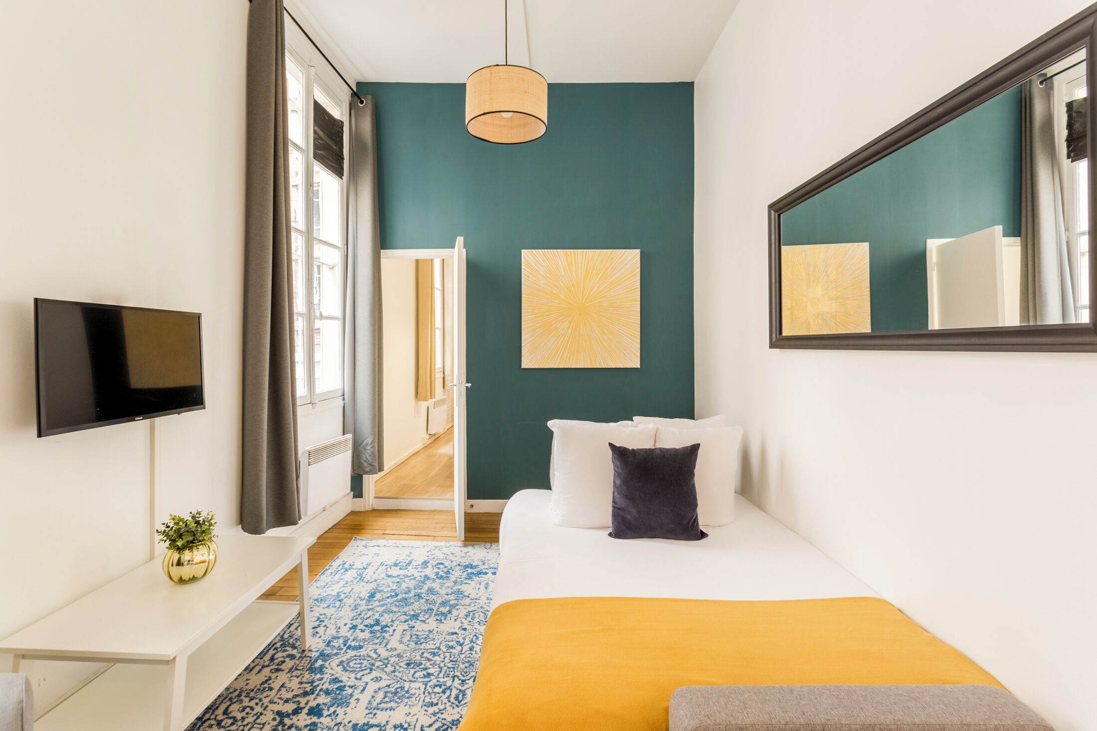 A modern hotel room with a bed, a TV, a desk, and a large mirror.
