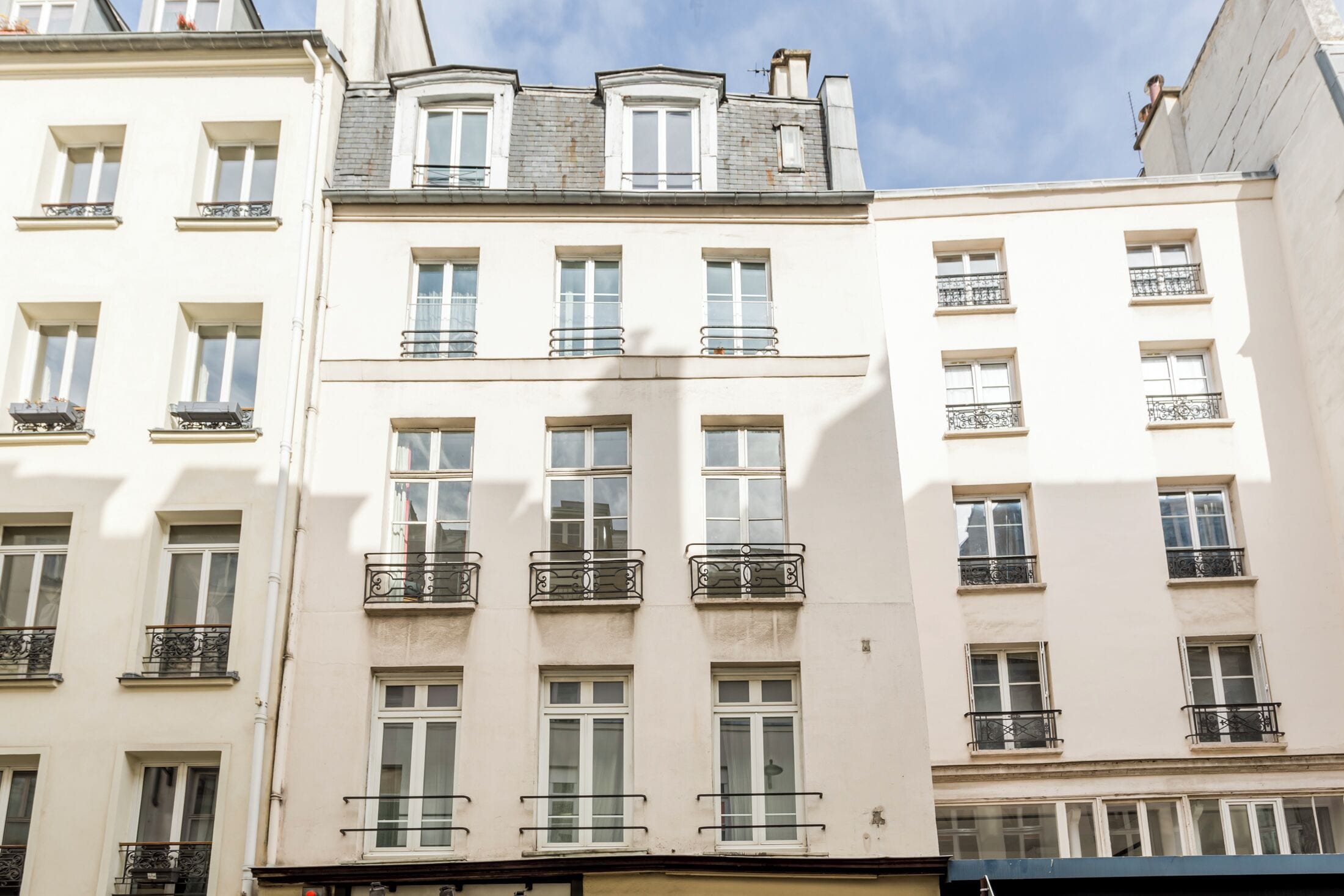 A multi-story building with white facades, multiple balconies, and a clear sky.