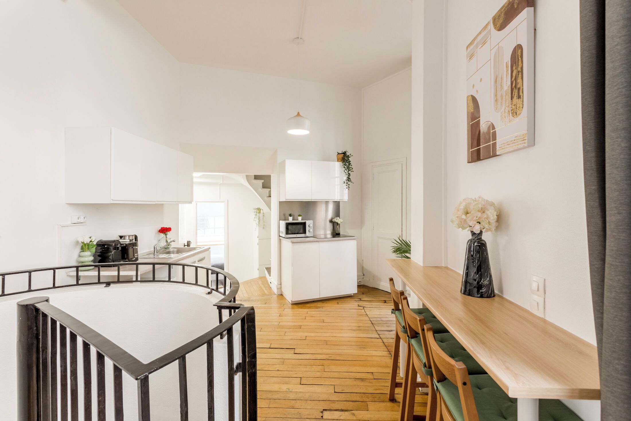 Une cuisine moderne avec des meubles blancs, une table à manger en bois et un escalier menant à une autre pièce.