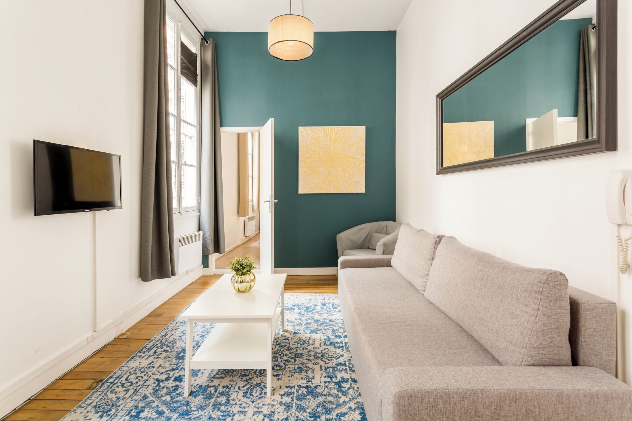 Un salon moderne avec un canapé gris, une table basse blanche et un tapis à motifs bleus.