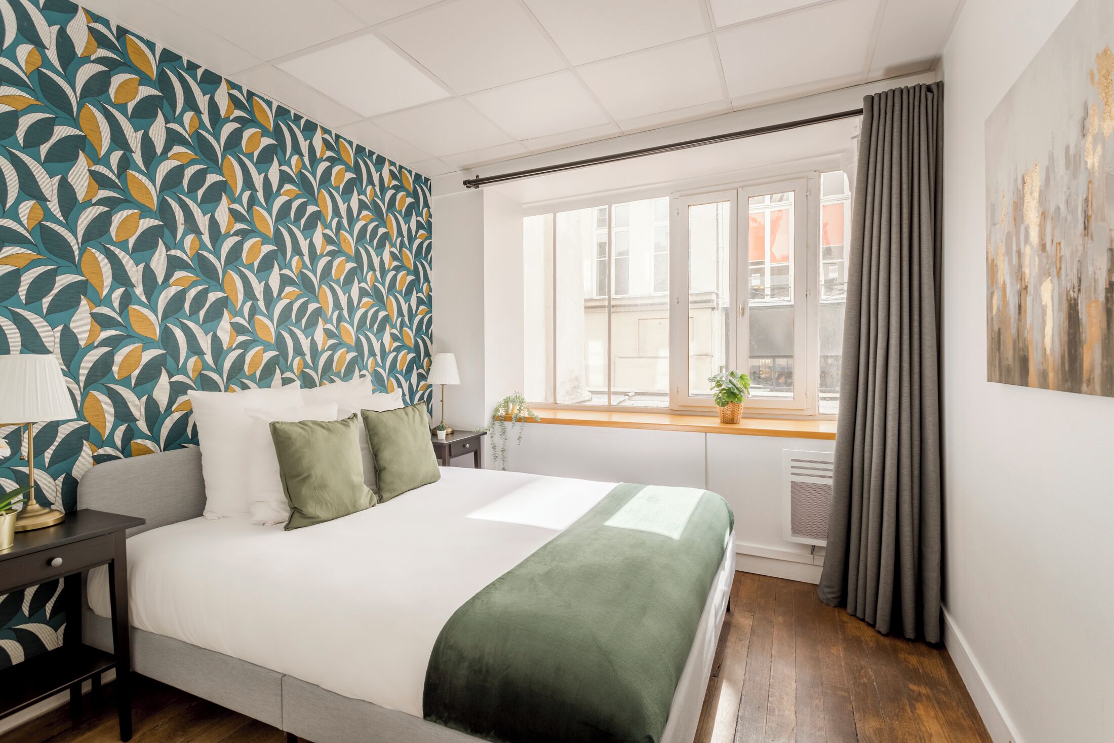 A bedroom with a bed, a nightstand, a lamp, a window with curtains, and a patterned wall.