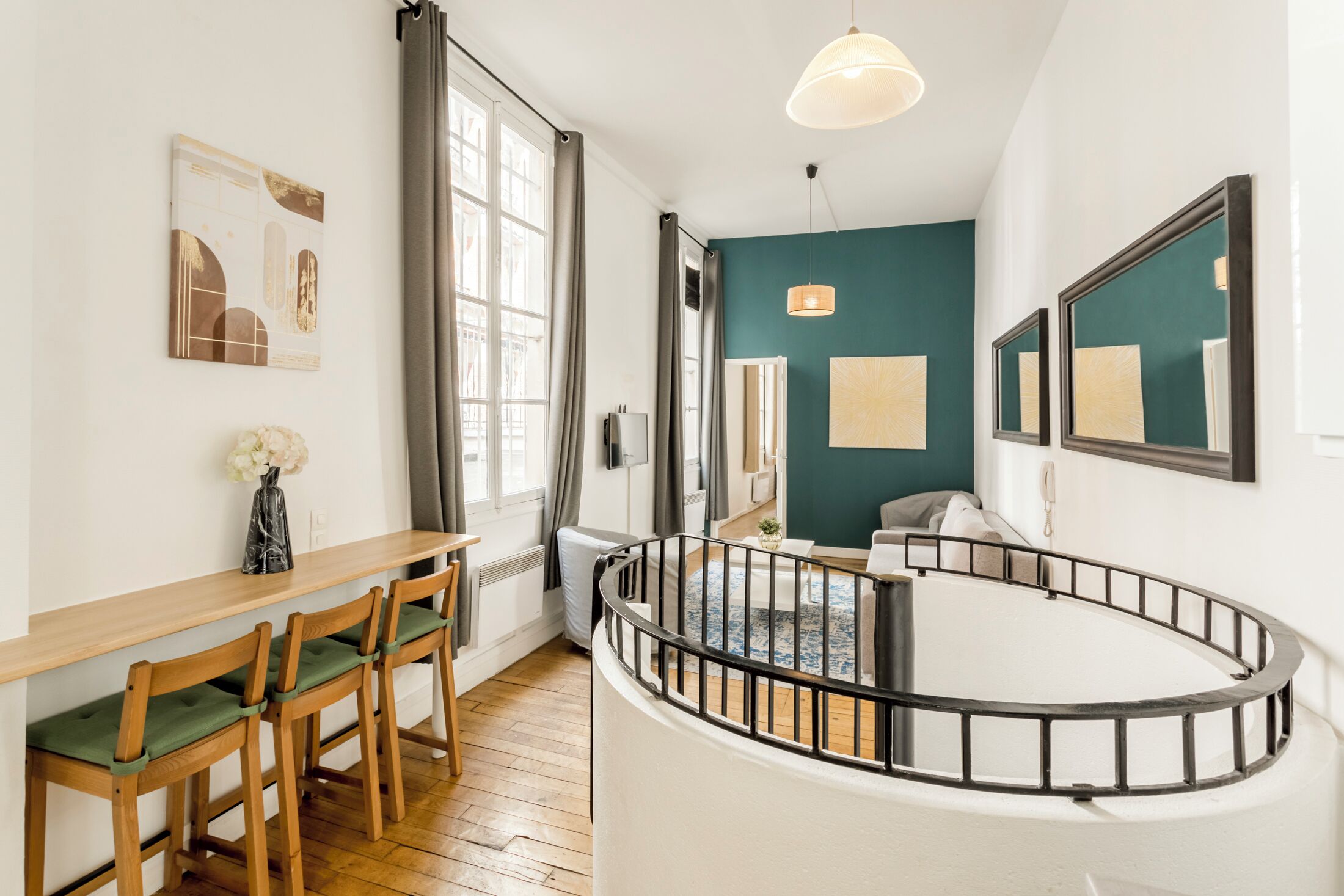 A modern living room with a curved staircase, a dining area with wooden chairs and a table, and artwork on the walls.