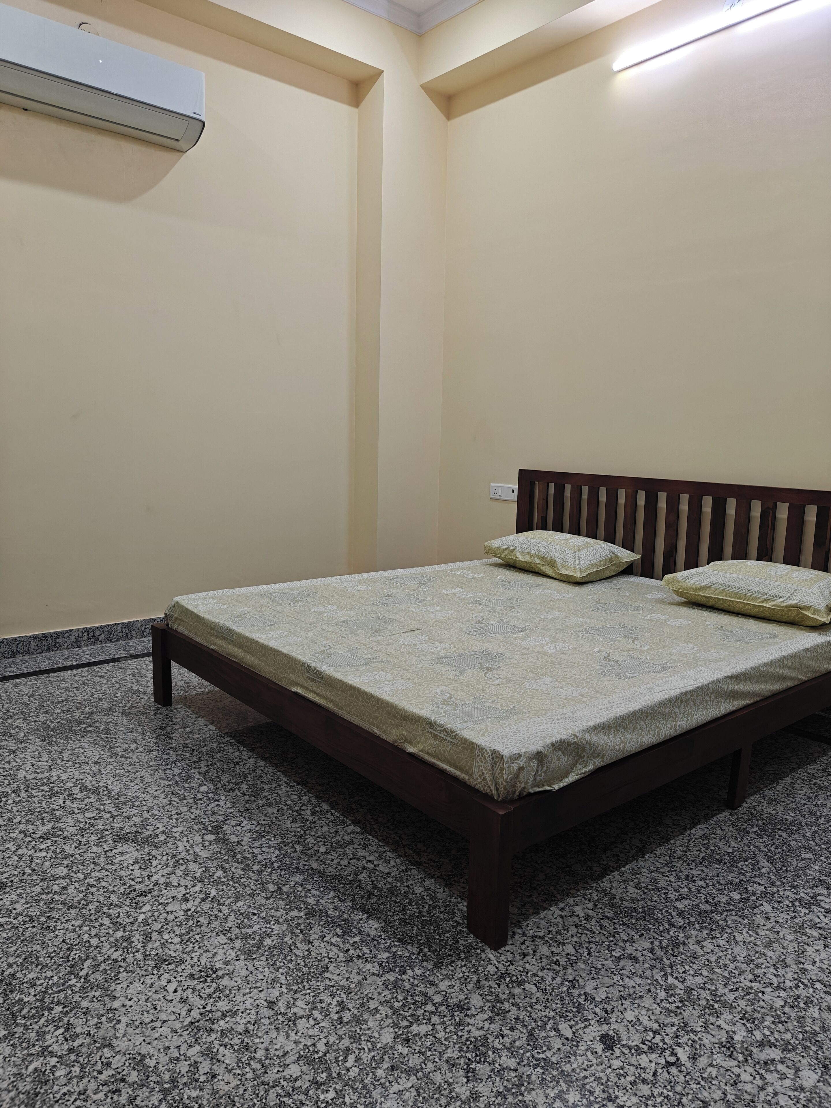 A room with a bed, a wooden headboard, a wall-mounted air conditioner, and a textured floor.