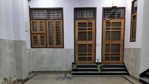 Un pasillo con tres puertas y ventanas de madera, suelo de baldosas y una cámara de seguridad en el techo.