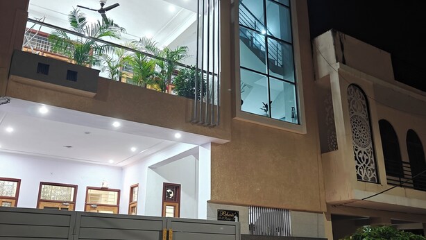 Un edificio moderno de dos pisos con un balcón grande, entrada protegida por una reja y un interior bien iluminado.