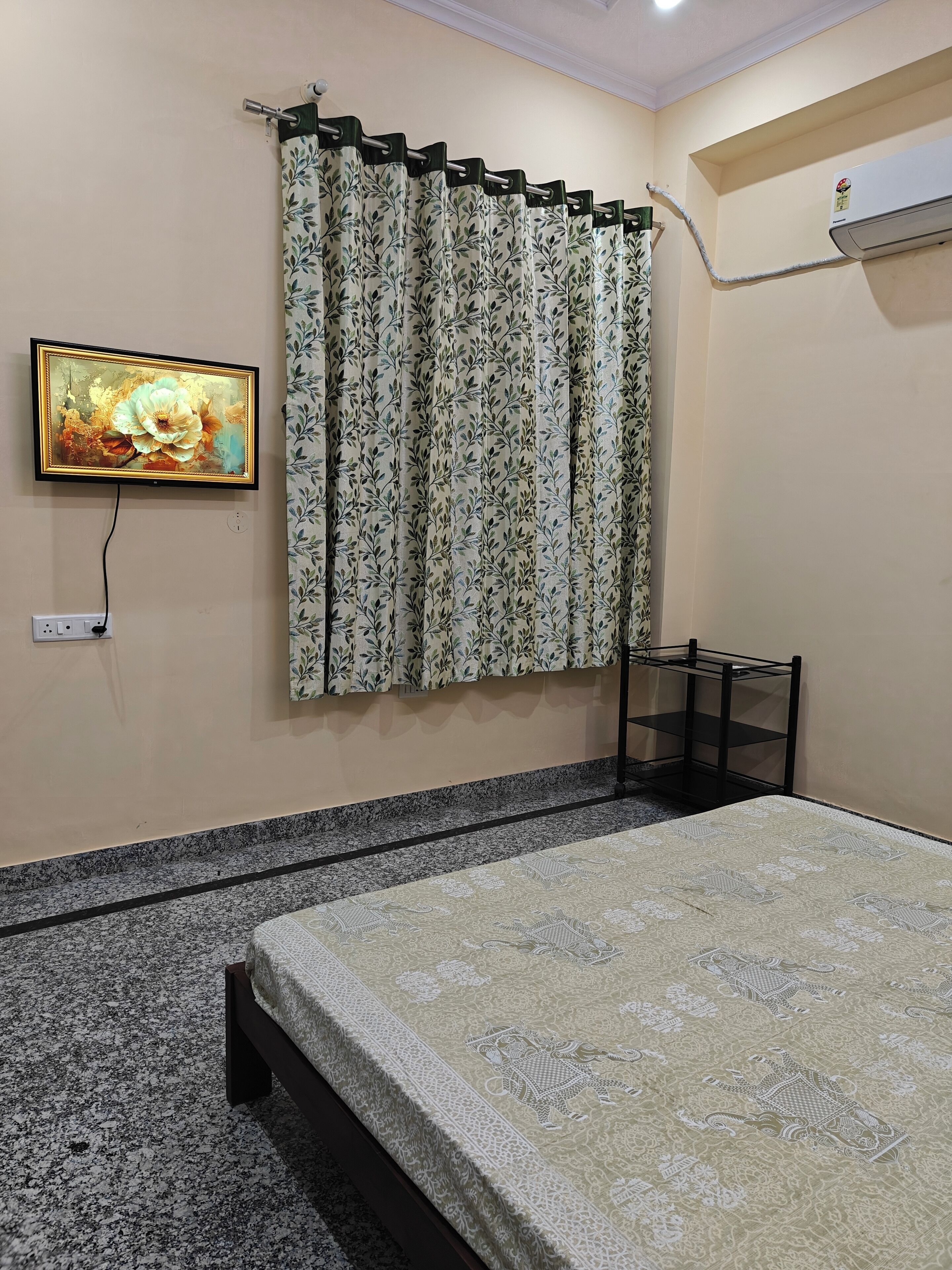 A bedroom with a bed, a TV mounted on the wall, a curtain, and a shelf unit.