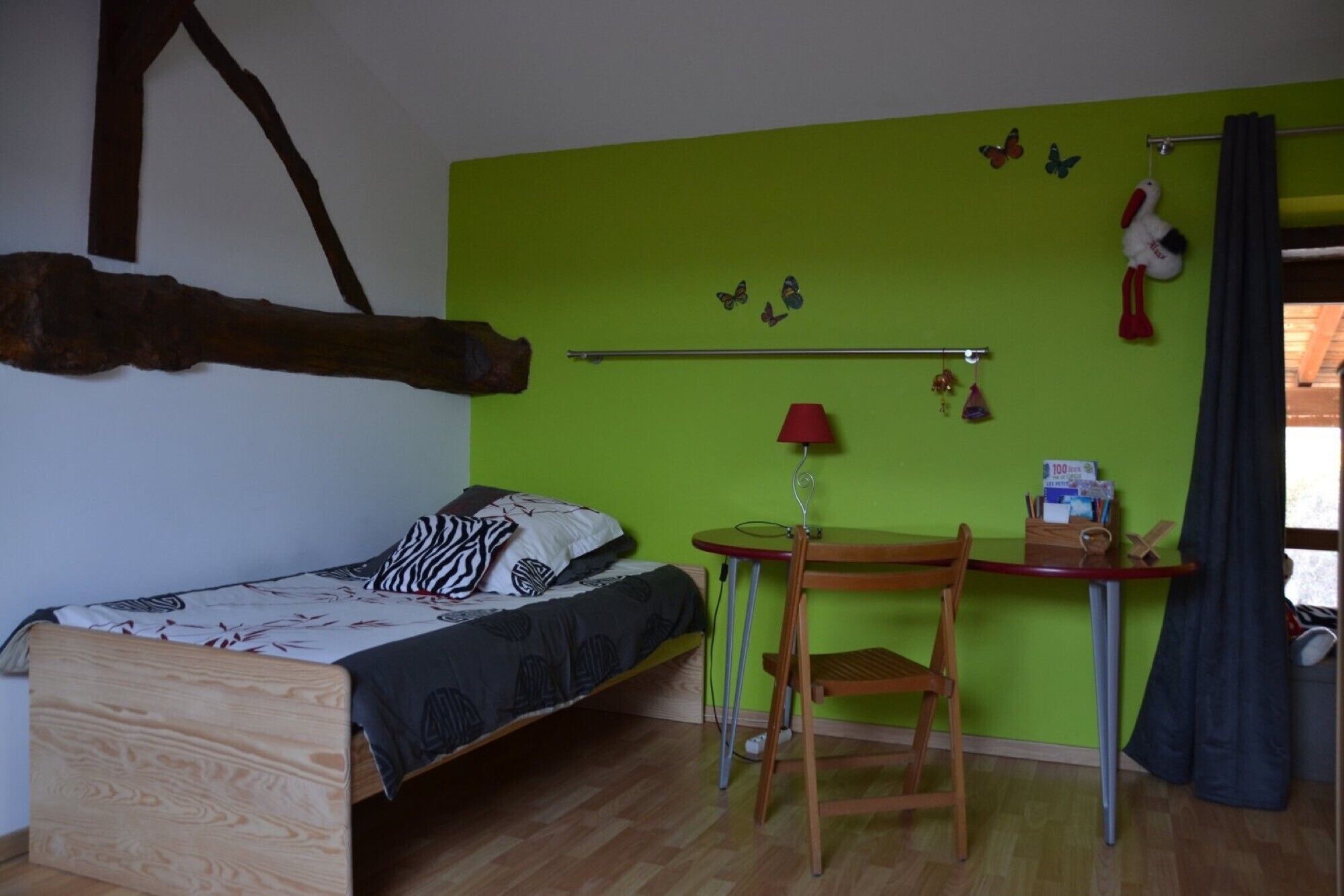 A room with a bed, a desk, a chair, a lamp, and a window with curtains.