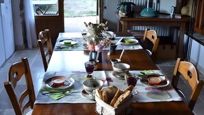 A dining table set with plates, bowls, and bread, with chairs around it.
