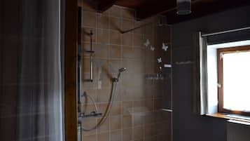 Une douche avec une porte en verre, une fenêtre donnant sur un beau paysage et un mur carrelé.