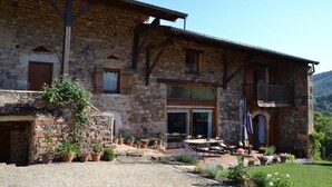 A stone building with a balcony, a covered patio with outdoor seating, and potted plants.