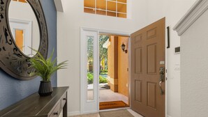 A hallway with a wooden door, a welcome mat, a potted plant, and a wall-mounted mirror. - ⭐⭐Spacious 6 bed Home | Gated Resort | Netflix Den | PS5 | Conservation View⭐⭐ (Davenport)