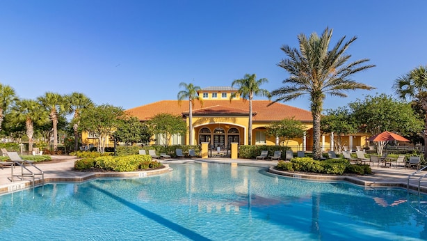 A swimming pool with lounge chairs and palm trees, surrounded by buildings with a yellow facade and red-tiled roofs. - ⭐⭐Spacious 6 bed Home | Gated Resort | Netflix Den | PS5 | Conservation View⭐⭐ (Davenport)