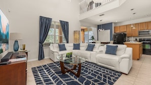 A modern living room with a glass coffee table, white sofa, and a view of the kitchen. - ⭐⭐Spacious 6 bed Home | Gated Resort | Netflix Den | PS5 | Conservation View⭐⭐ (Davenport)
