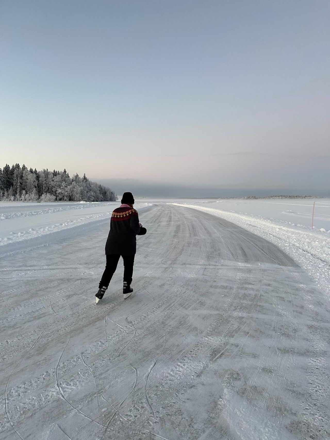 A person ice skating on a frozen lake with trees in the background.