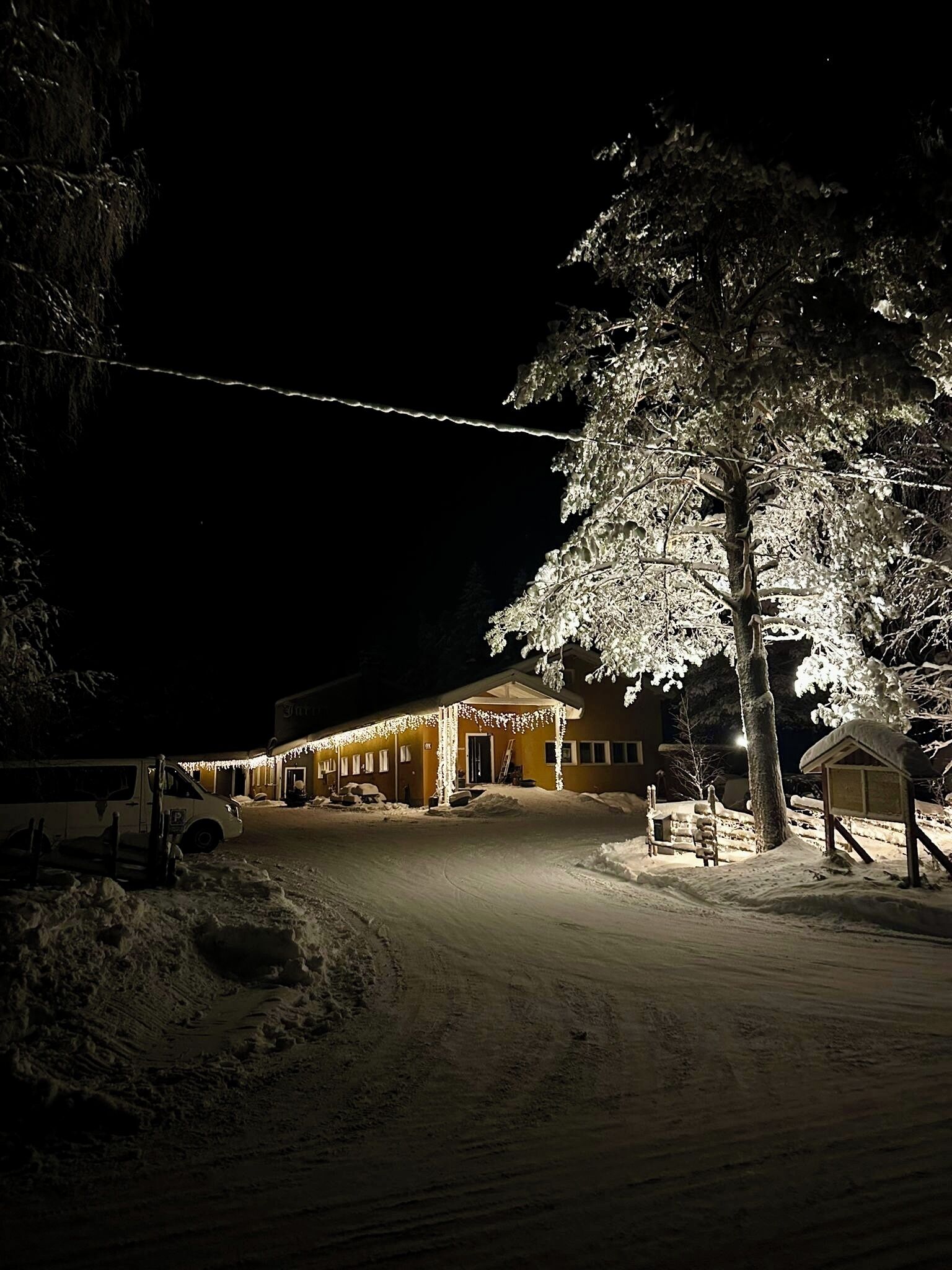 Lumipeitteinen maisema, jossa on rakennus, jossa on katettu kuisti ja opastekyltti.