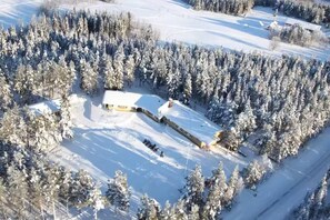 Ett flygbildsfoto av en snötäckt skog med en liten byggnad omgiven av träd.
