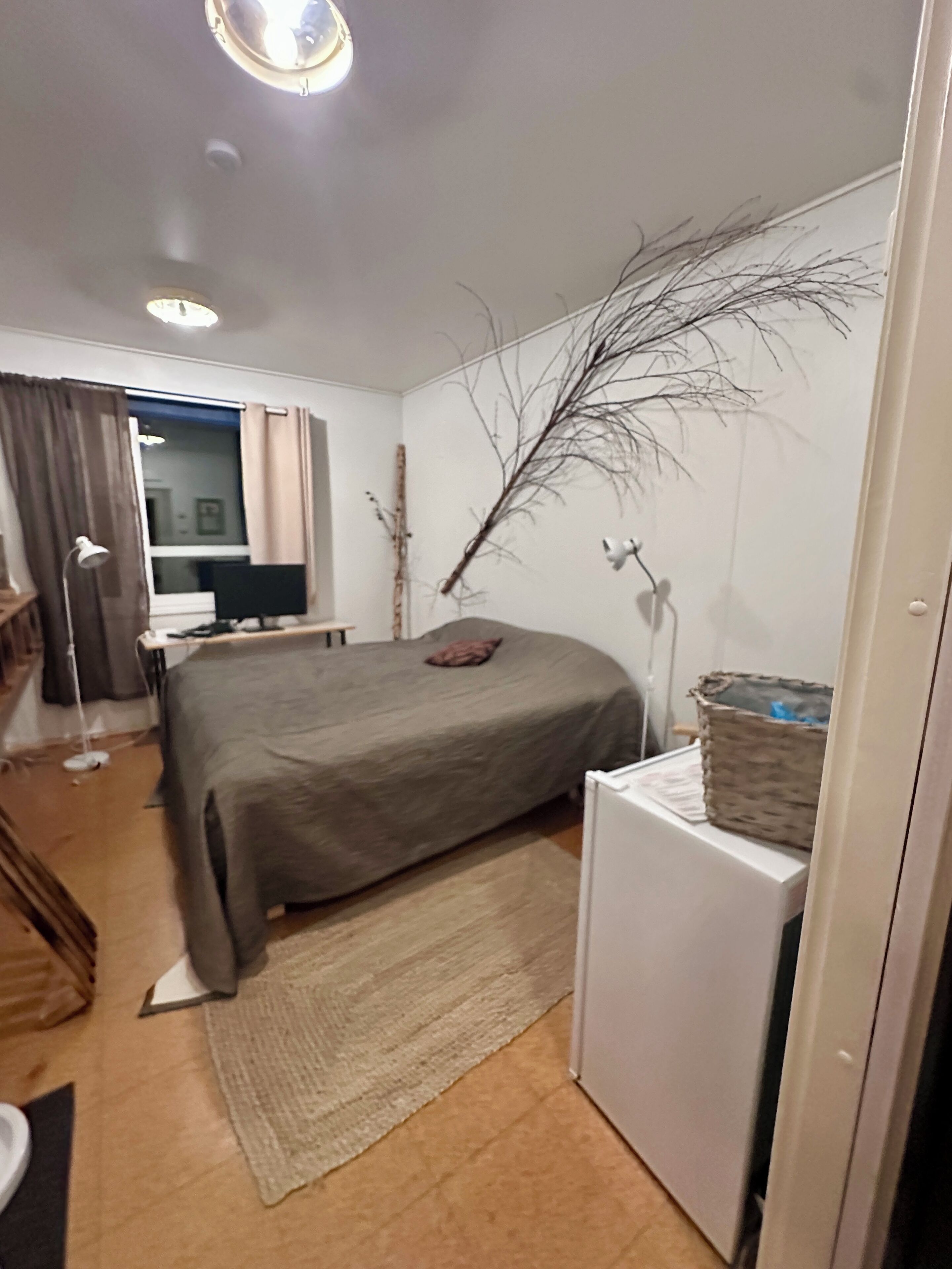 A bedroom with a bed, a desk, a chair, a lamp, a TV, and a window with curtains.