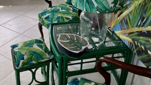 A green chair with a glass seat and backrest, surrounded by a tropical leaf-patterned cushion.