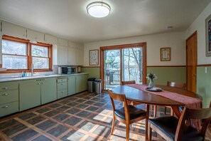 A kitchen with a dining table, chairs, a microwave, and a view through the glass door. - Creekside Cottage! Lake Altoona Getaway (Eau Claire)