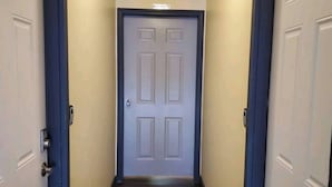 Um corredor com piso de madeira, portas brancas com detalhes em azul e uma luminária no teto.