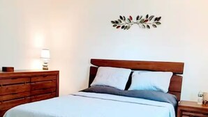 Quarto com estrutura de cama de madeira, colcha branca e mesa de cabeceira com abajur.