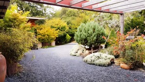 A gravel pathway leading through a garden with various plants and a wooden pergola structure. - Gîte Dilos – Holiday Home in Gan (Gan)