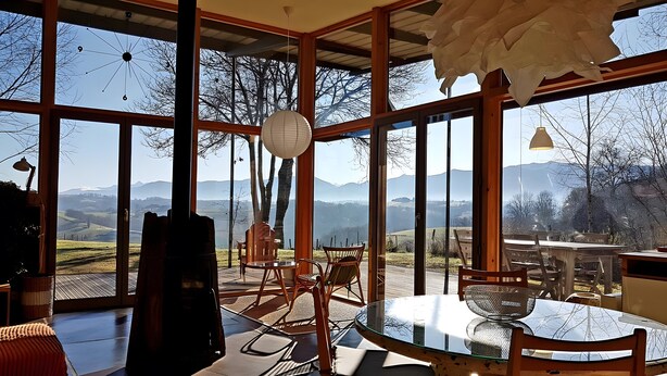 A spacious room with large windows offering a mountain view, a glass table, and wicker chairs. - Gîte Dilos – Holiday Home in Gan (Gan)